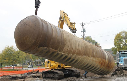 Three construction workers wearing safety vests and hard hats reviewing blueprints together on a job site.