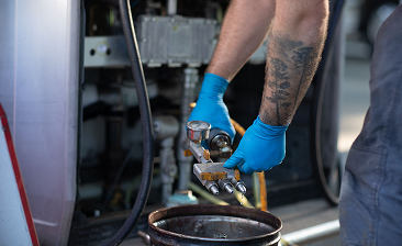Person wearing blue gloves holding a fuel nozzle dispensing liquid into a container.