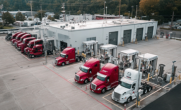 Concrete dock extending into a lake with trees in the background and fuel dispenser pump on the right.
