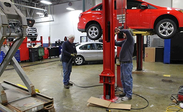 Worker in an orange shirt and blue gloves inspecting pipes in a fuel dispenser/forecourt.