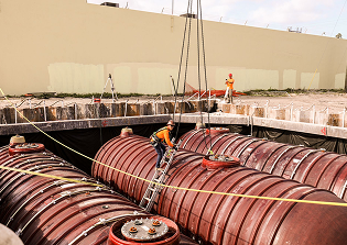 Concrete dock with mooring cleats extending into a lake surrounded by trees under a partly cloudy sky.