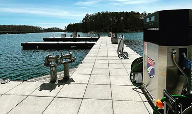 Pier with boat fueling station and cleats along calm lake under blue sky.