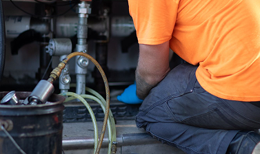 Technician in an orange shirt and blue gloves repairing plumbing under a sink.