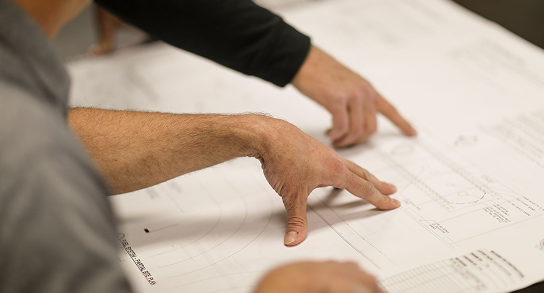 Two people pointing and discussing details on a large technical blueprint or architectural drawing.