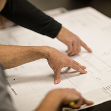 Two people pointing and discussing details on a large architectural blueprint.
