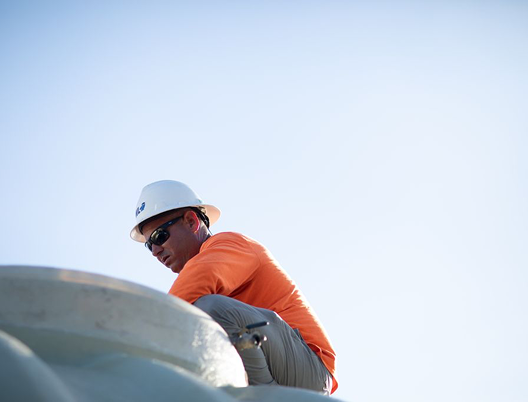 Person with tattooed arm reviewing large architectural blueprints on a wooden table.