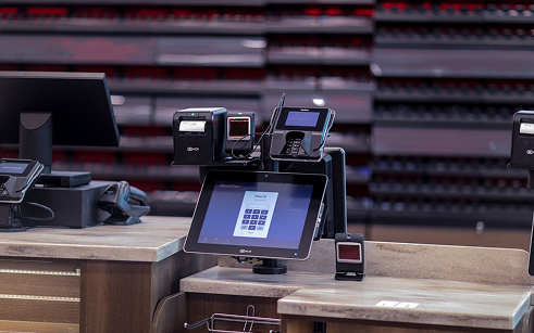 Modern retail checkout counter with touchscreen POS system, card reader, and receipt printer.