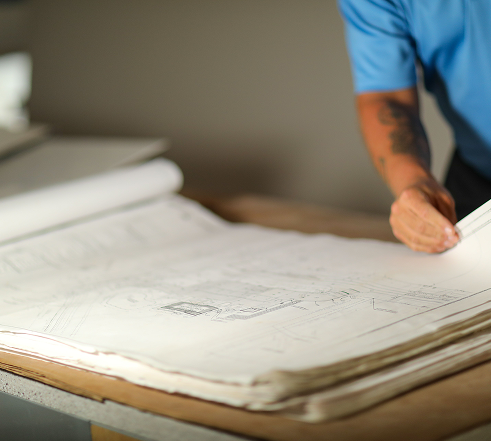 Person in blue shirt examining large architectural blueprints on a table.