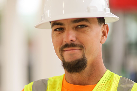 Construction worker wearing a white hard hat and yellow safety vest, smiling at the camera.
