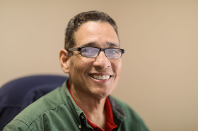 Smiling middle-aged man wearing glasses and a green shirt against a beige background.