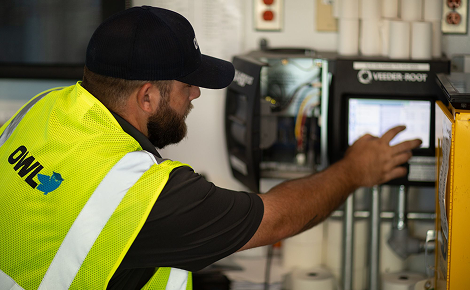 Technician wearing a black cap and yellow safety vest operating industrial equipment with a digital screen.