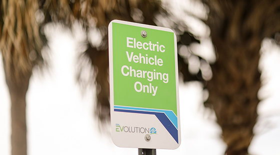 Bearded man wearing glasses, a blue polo shirt with a logo, and earphones, looking to the side indoors.