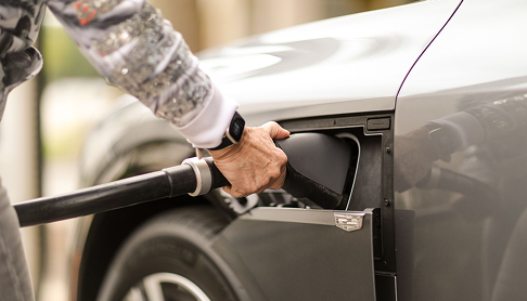 Person refueling a gray car by inserting a gas pump nozzle into the fuel tank.