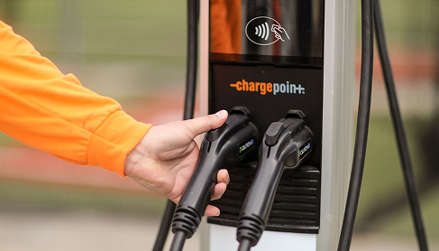 Hand in orange sleeve plugging an electric vehicle charger into a ChargePoint station.