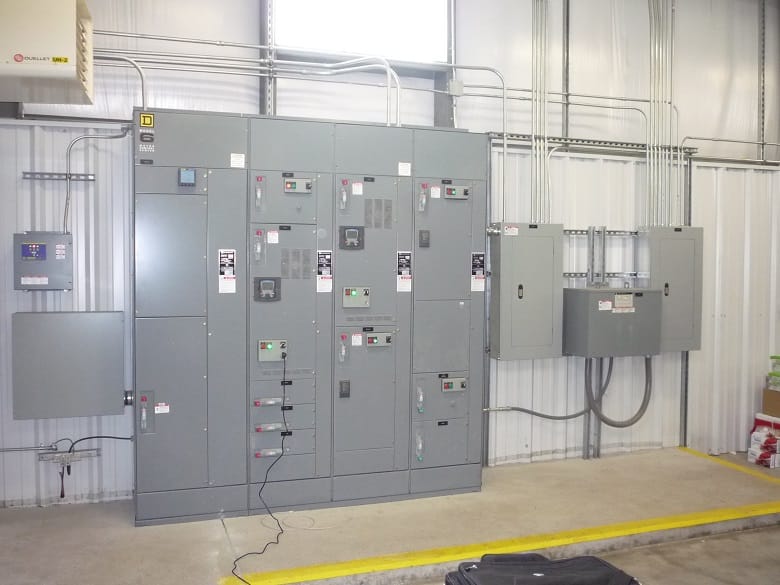 Industrial electrical control panels mounted on a white metal wall with multiple conduit pipes running vertically and horizontally.
