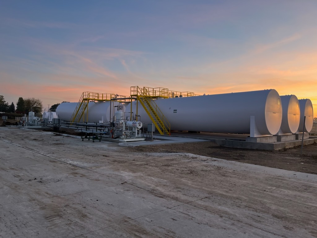 Large white industrial storage tanks with yellow staircases at an outdoor facility during sunset.