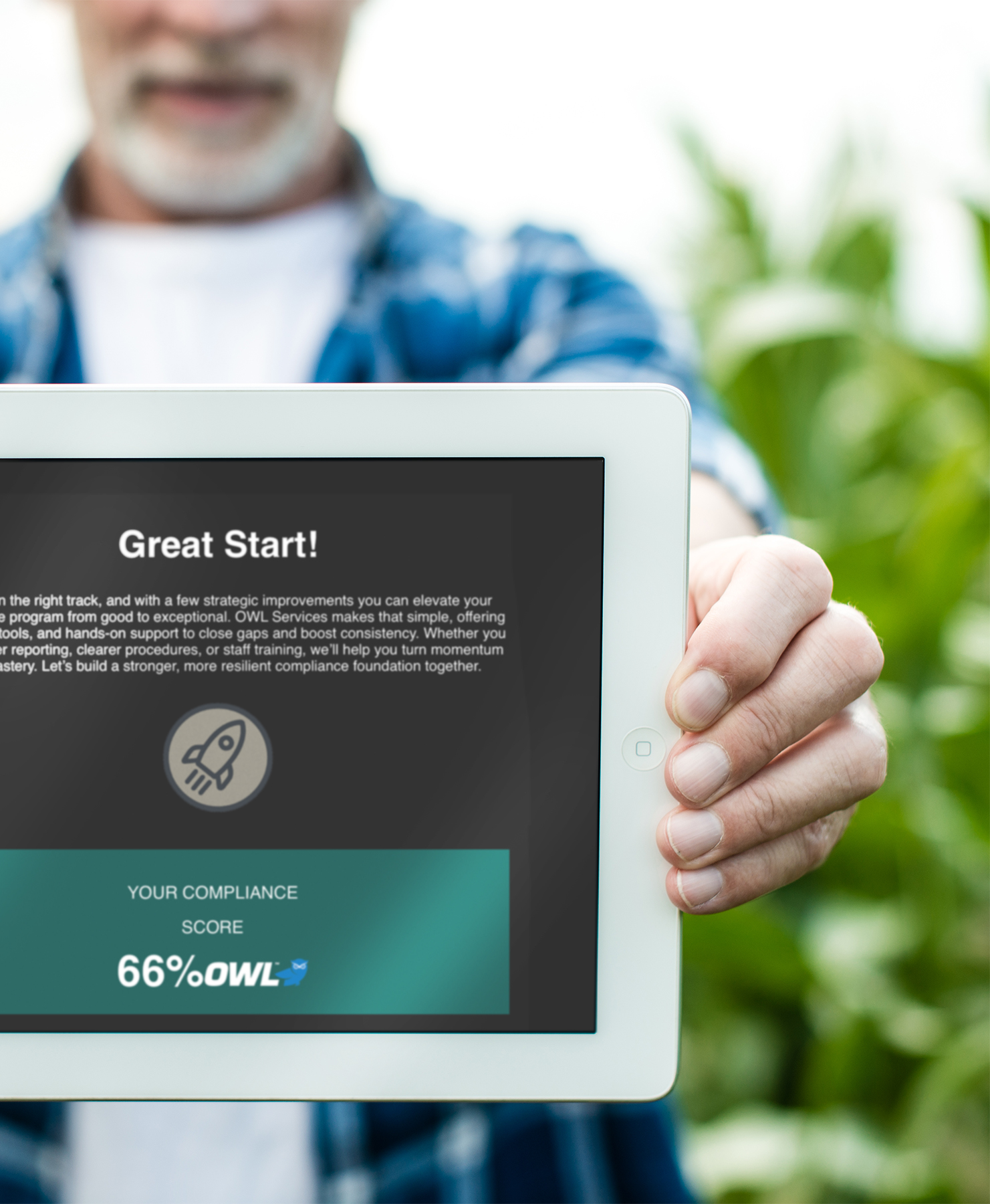 Close-up of a person holding a tablet showing a compliance score of 66% with a rocket icon and text starting with 'Great Start!'