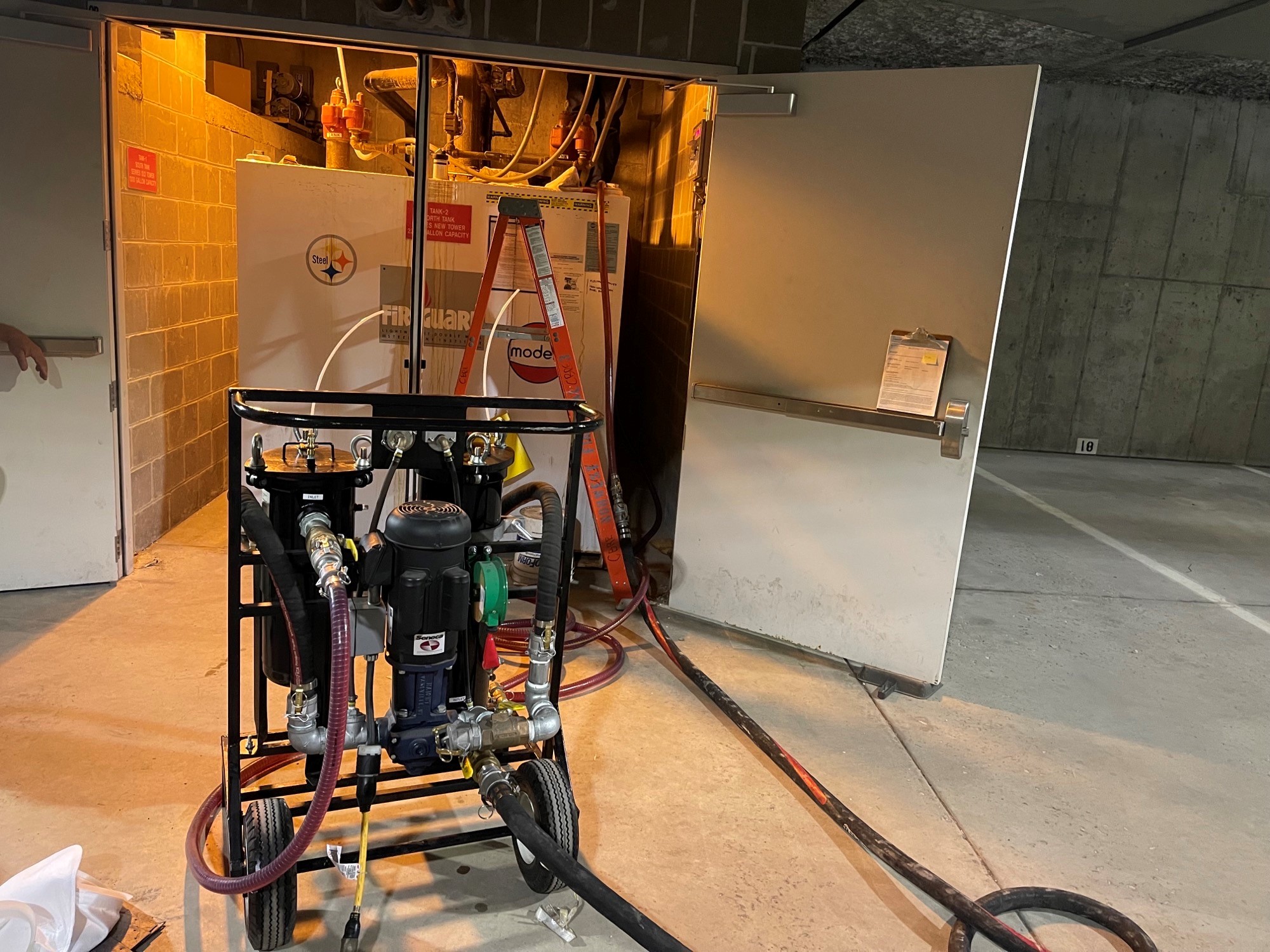 Industrial fuel filtration equipment with hoses set up in a lit utility room with open doors.