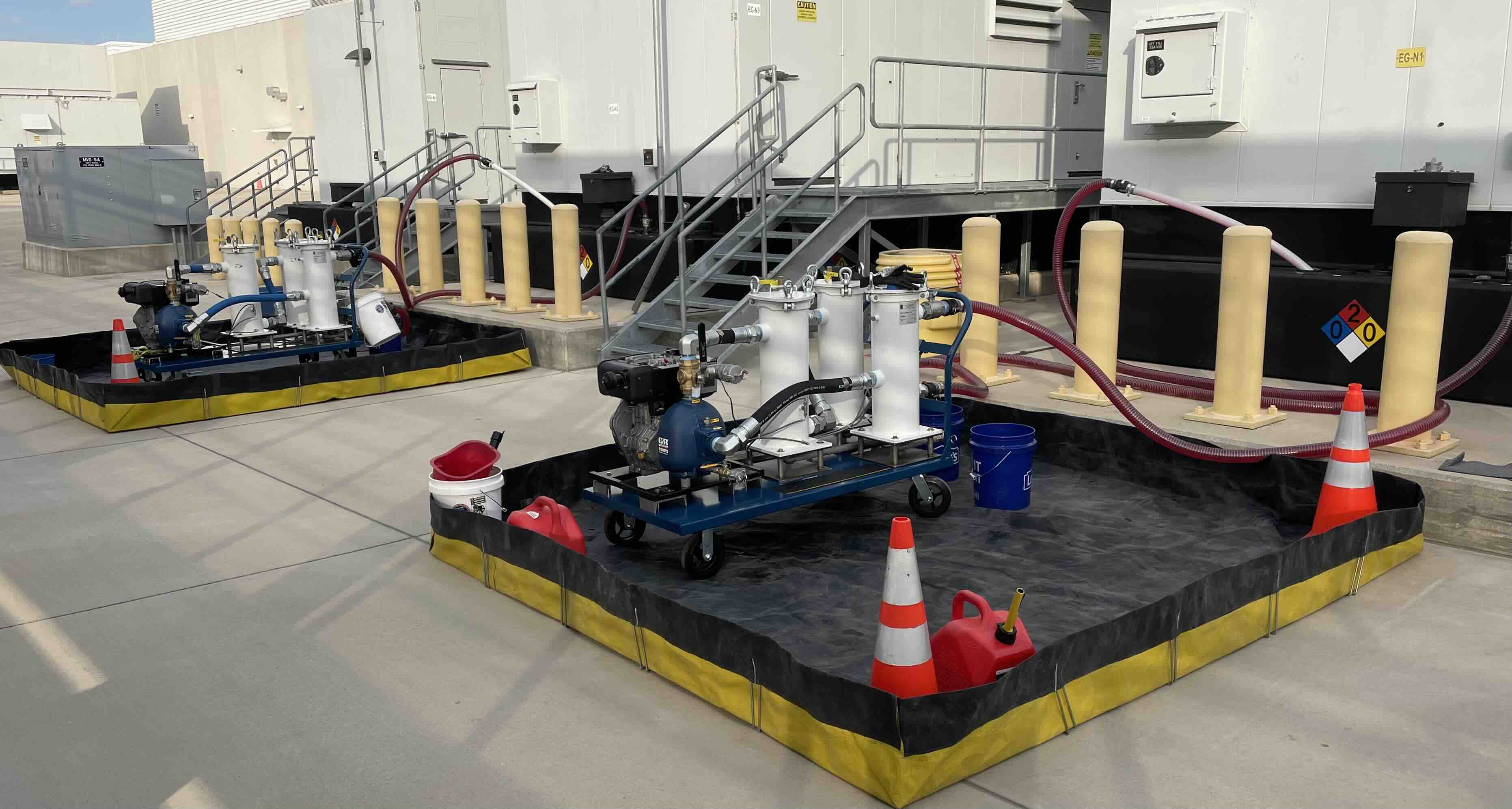 Two fuel filtration systems with pumps and hoses set up inside spill containment berms near an industrial building.