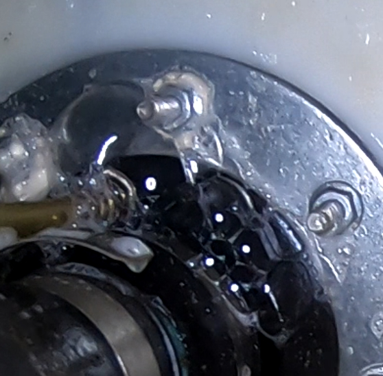 Close-up of a mechanical component with water droplets and a metal ring secured by bolts.