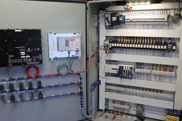 Open industrial electrical control panel with wiring, relays, circuit breakers, and electrical components neatly arranged.