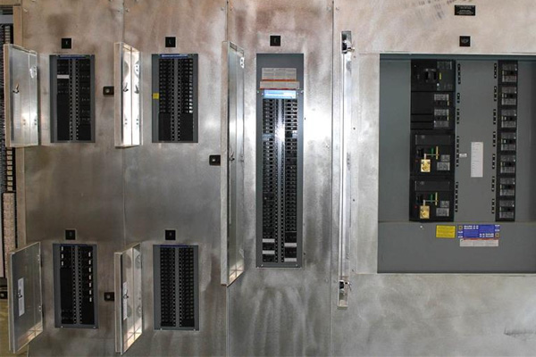 Metal electrical control panel with multiple circuit breaker compartments and open doors.