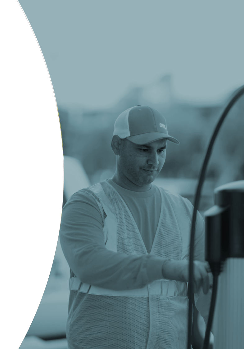 Man wearing a cap and safety vest operating an electric vehicle charging station.