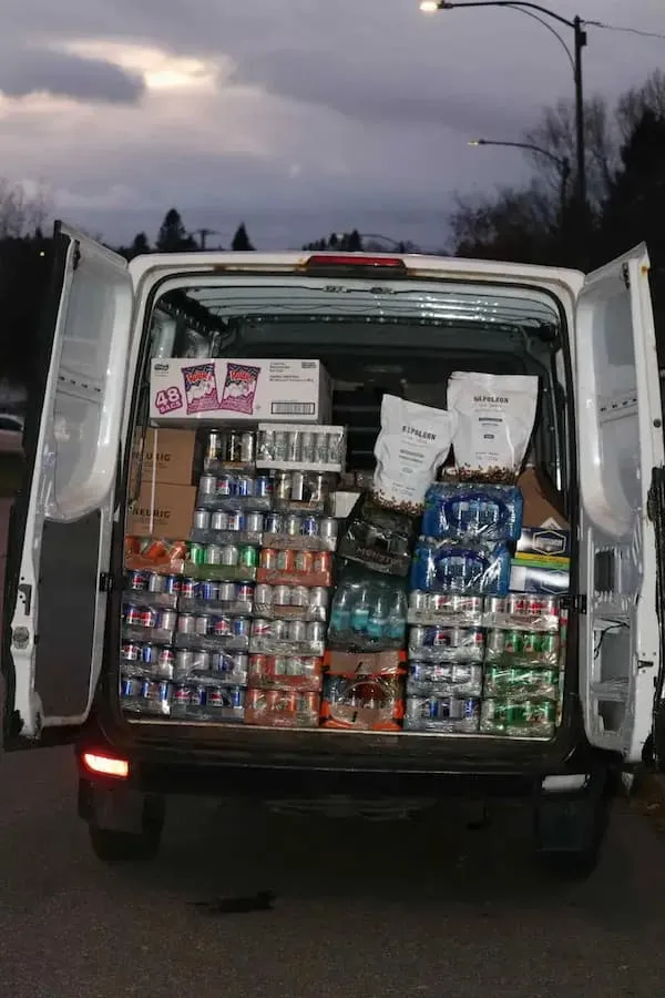 Fourgon blanc avec les portes arrière ouvertes rempli de boissons en canettes et cartons la nuit.