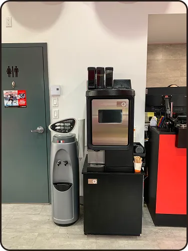 Distributeur de café noir avec souffleuse d'eau à côté dans une aire de repos intérieure.