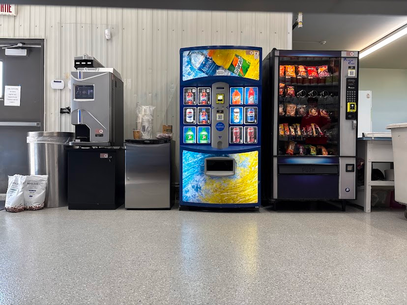 Machine à café automatique avec écran tactile, horloge murale et évier dans une cuisine.