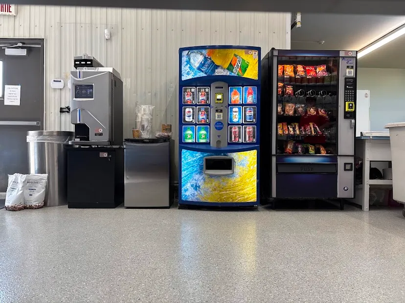 Machine à café automatique avec écran tactile, horloge murale et évier dans une cuisine.