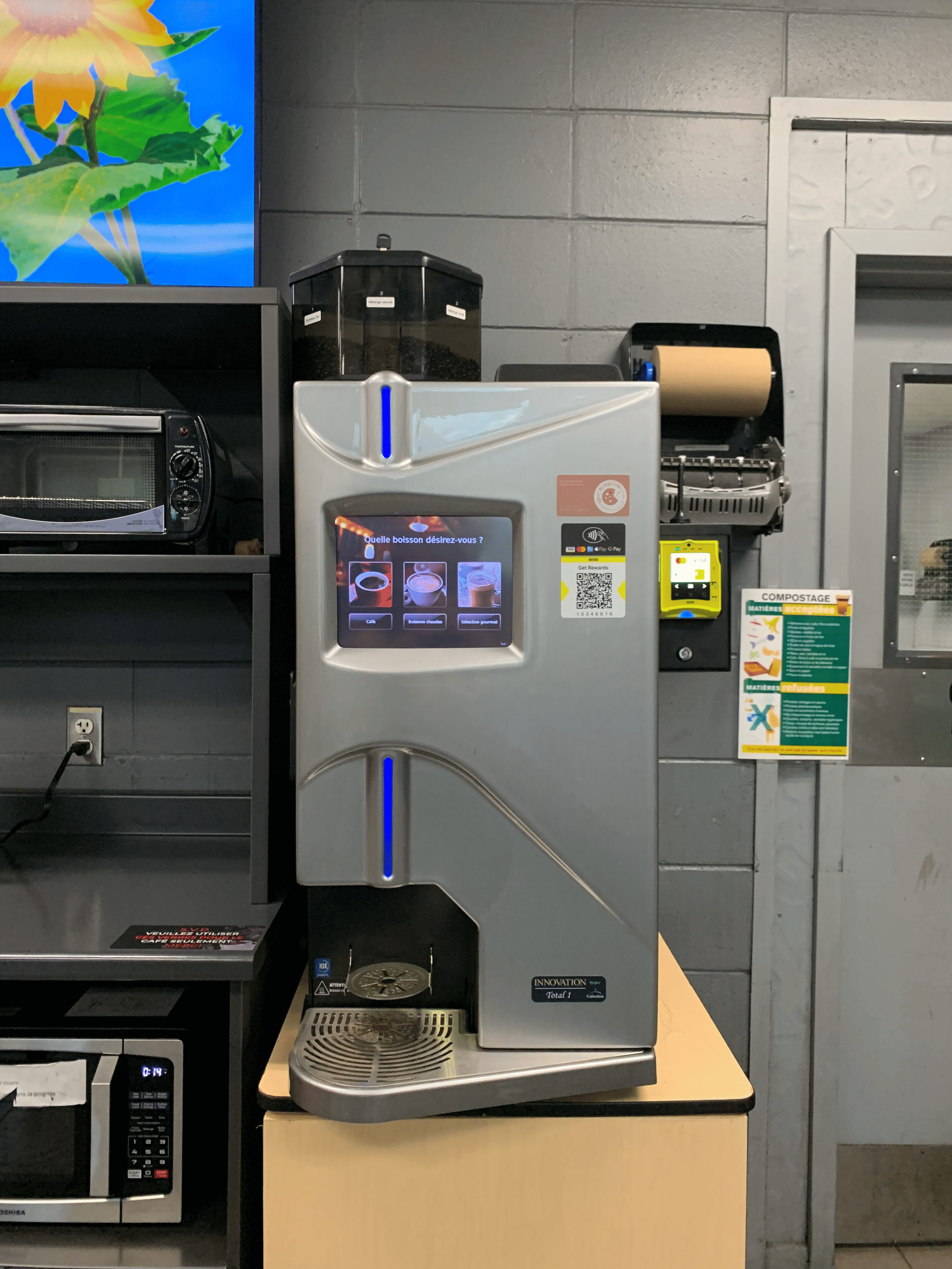 Machine à café automatique avec écran tactile affichant options de boissons en français dans une cuisine industrielle.