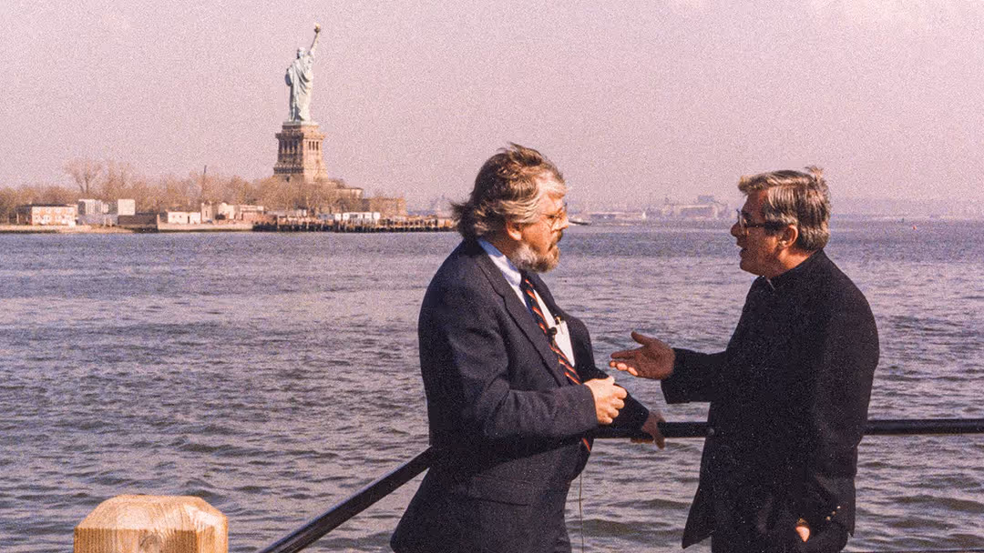 A priest talking with a CatholicTV host in New York City with the Statue of Liberty in the background