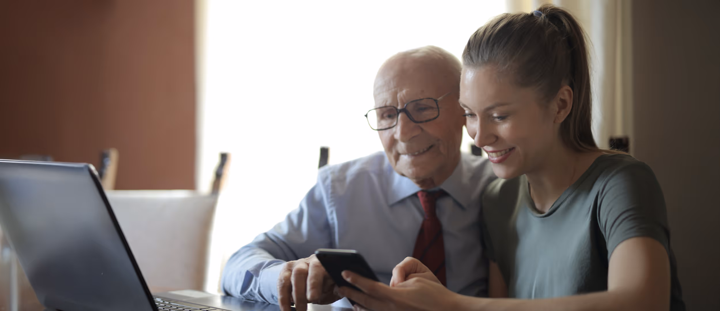 Young woman with her grandfather smiling and looking at his phone screen