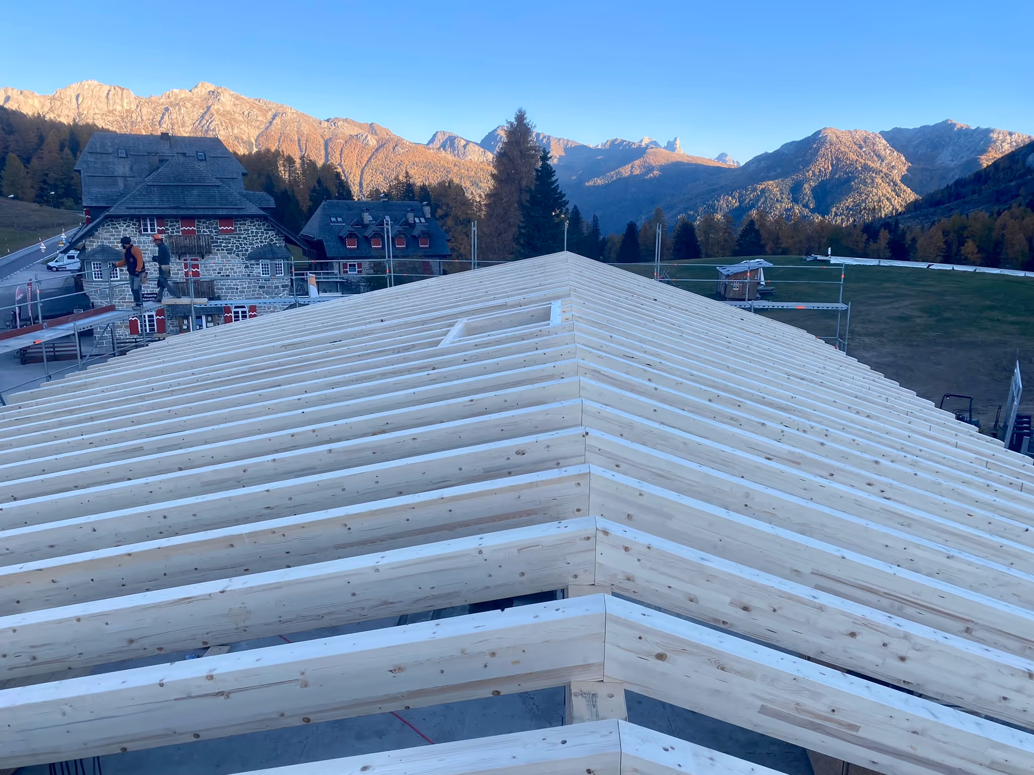 Dachstuhl eines neuen Holzhauses vor einer Berglandschaft mit Häusern und Bäumen bei klarem Himmel.