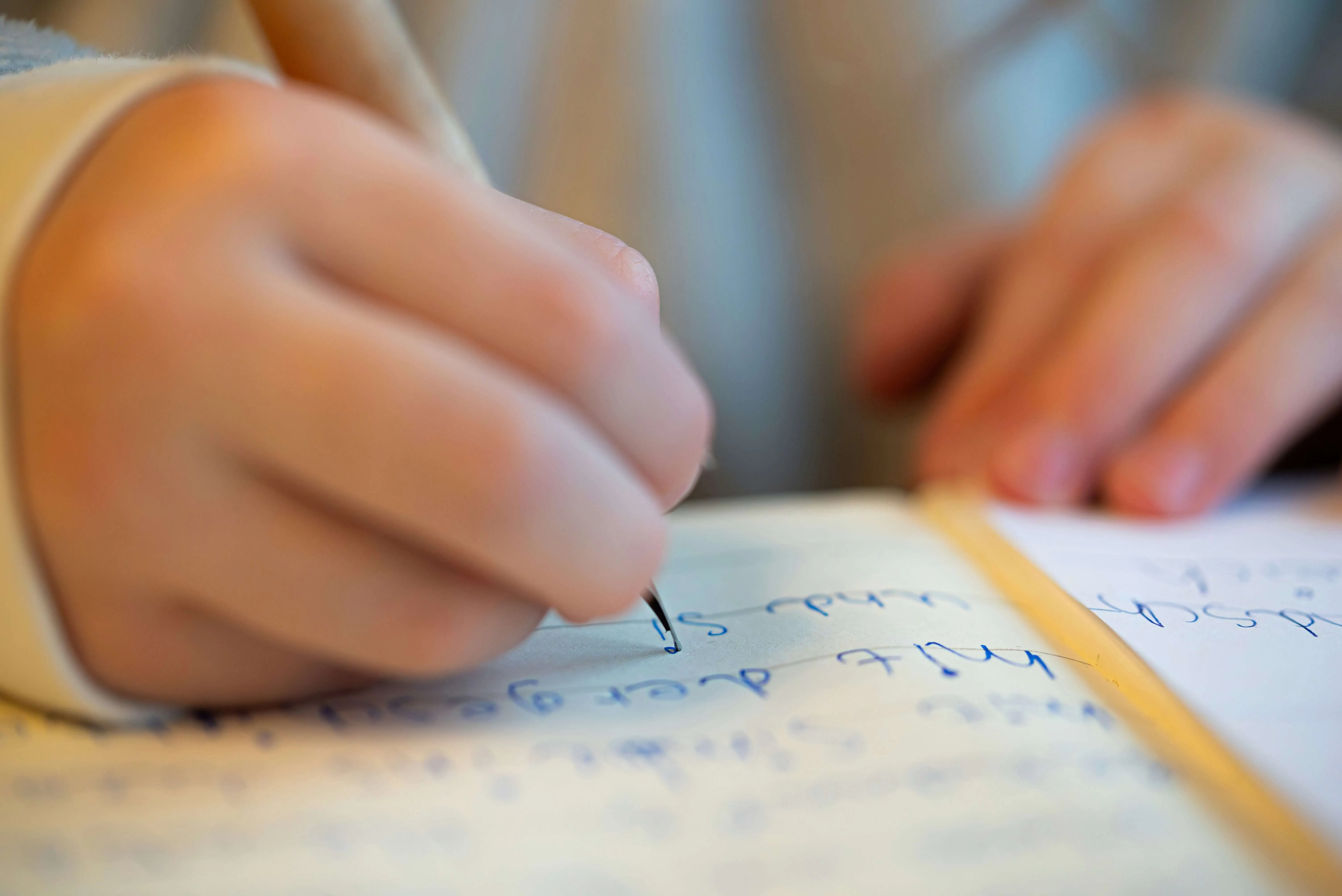Close-up of a person writing blue ink notes in a notebook.