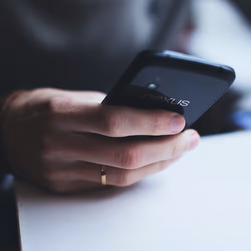 Close-up of a hand holding a black Nexus smartphone over a white surface.