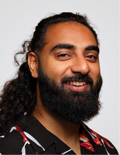 Smiling man with long curly hair and full beard wearing a black shirt with red and white floral pattern.