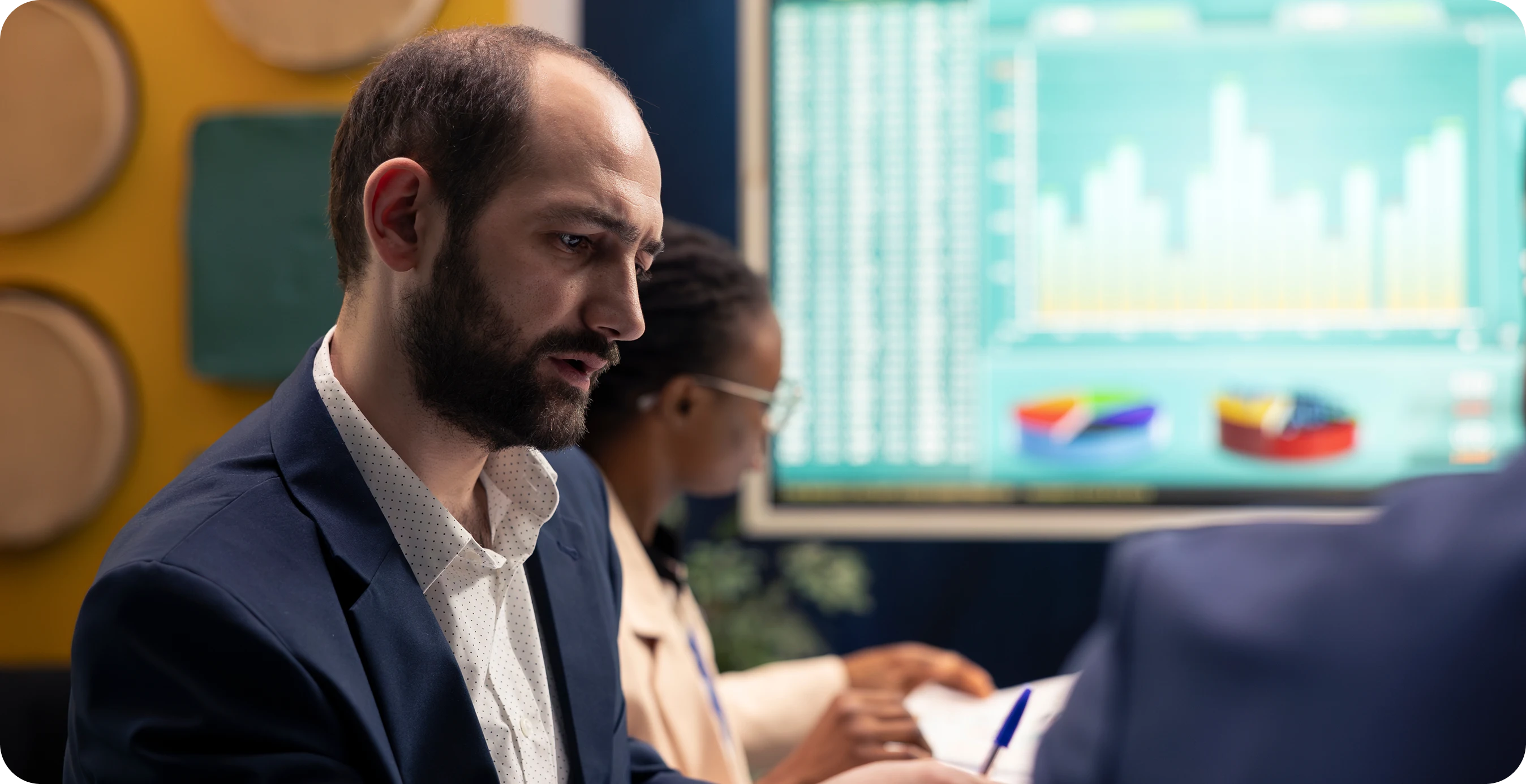 a man in a suit sitting in front of a screen