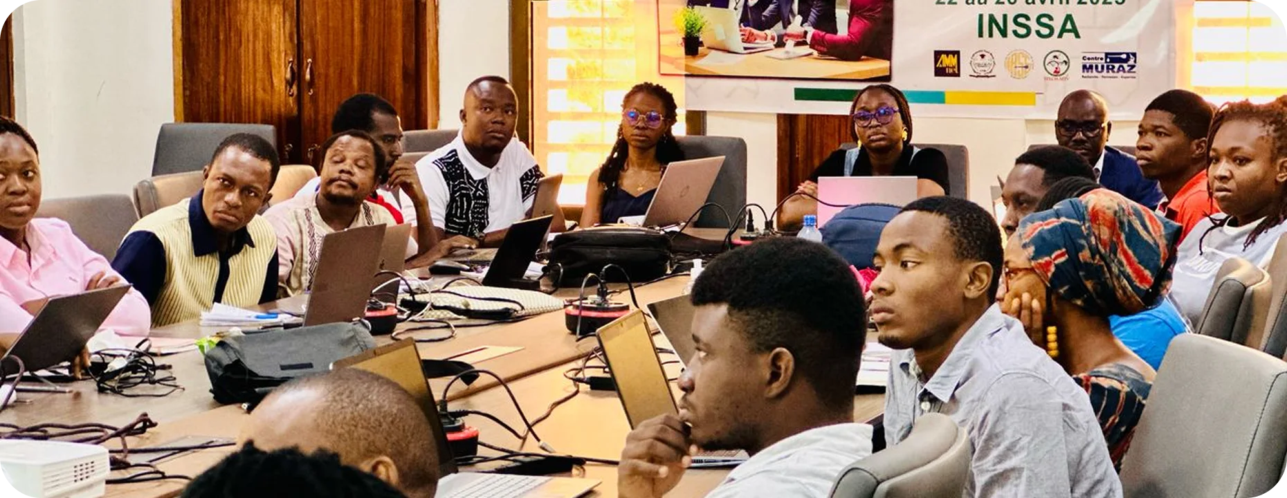 a group of people sitting around a table with laptops