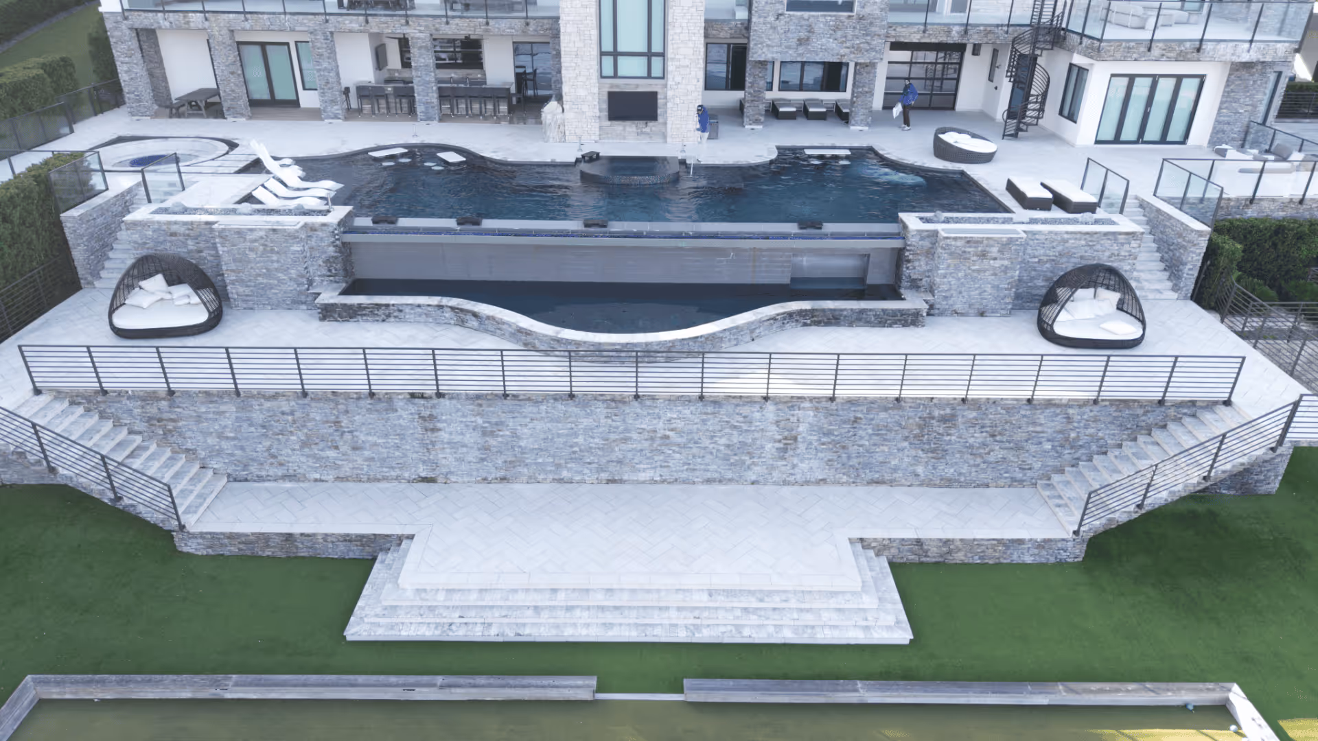 Modern luxury home backyard with an elevated infinity pool, sun loungers, and cushioned outdoor seating areas.