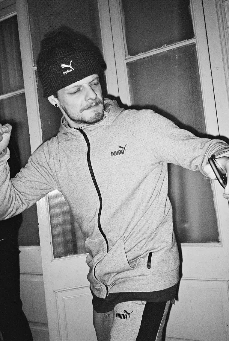 Man wearing Puma-branded beanie, zip-up hoodie, and sweatpants in a dynamic pose indoors.