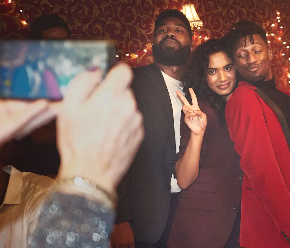 Three friends posing for a photo with one woman making a peace sign and two men standing closely, one in a red jacket.