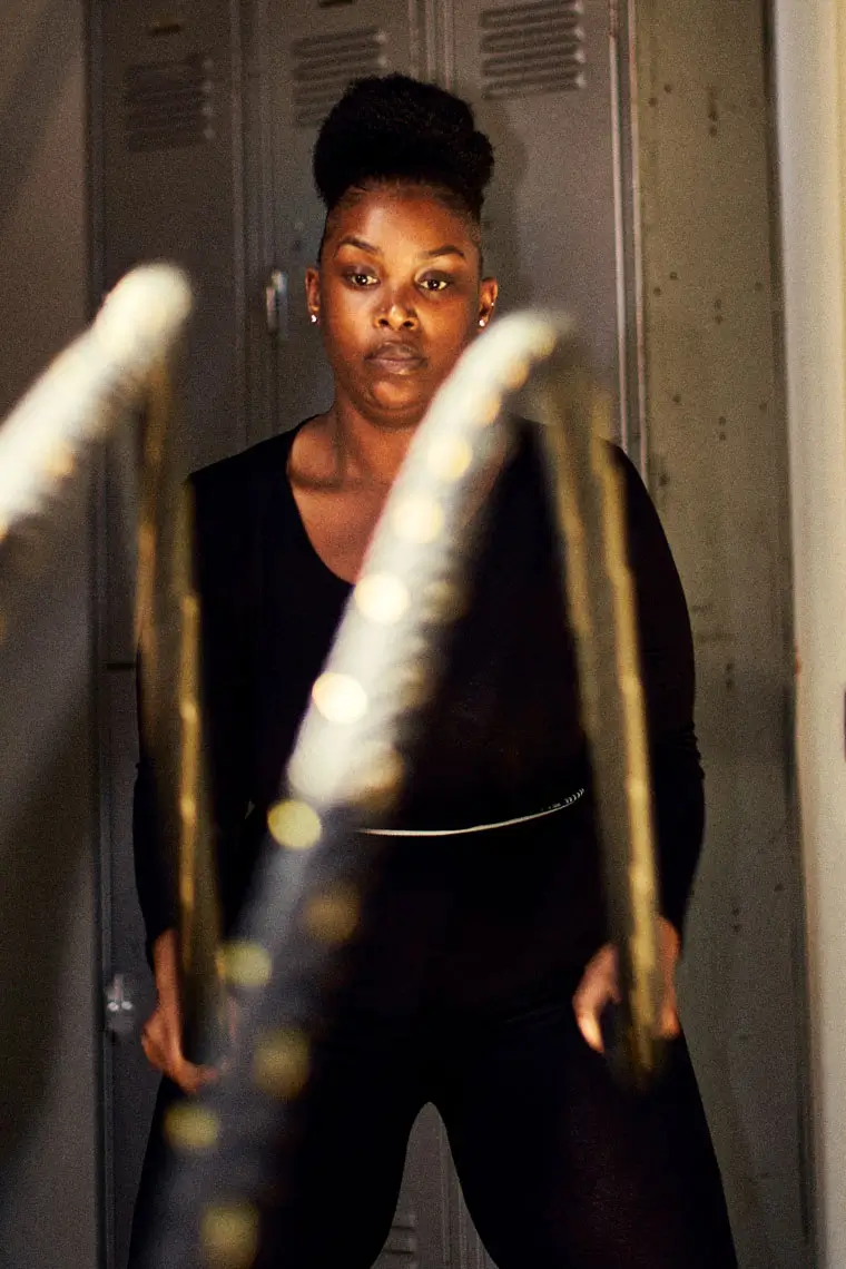 Woman with hair in a bun focused on intense battle rope workout in a gym locker room.