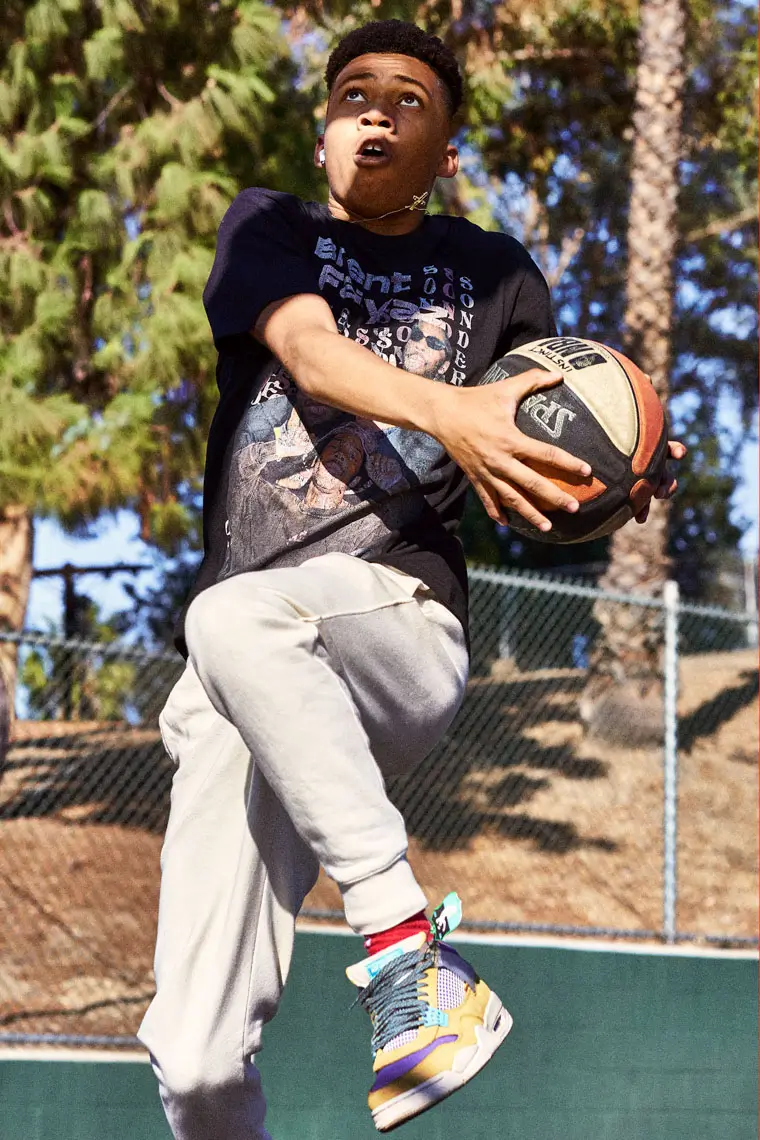 Young basketball player mid-air holding a basketball, preparing to make a layup outdoors.