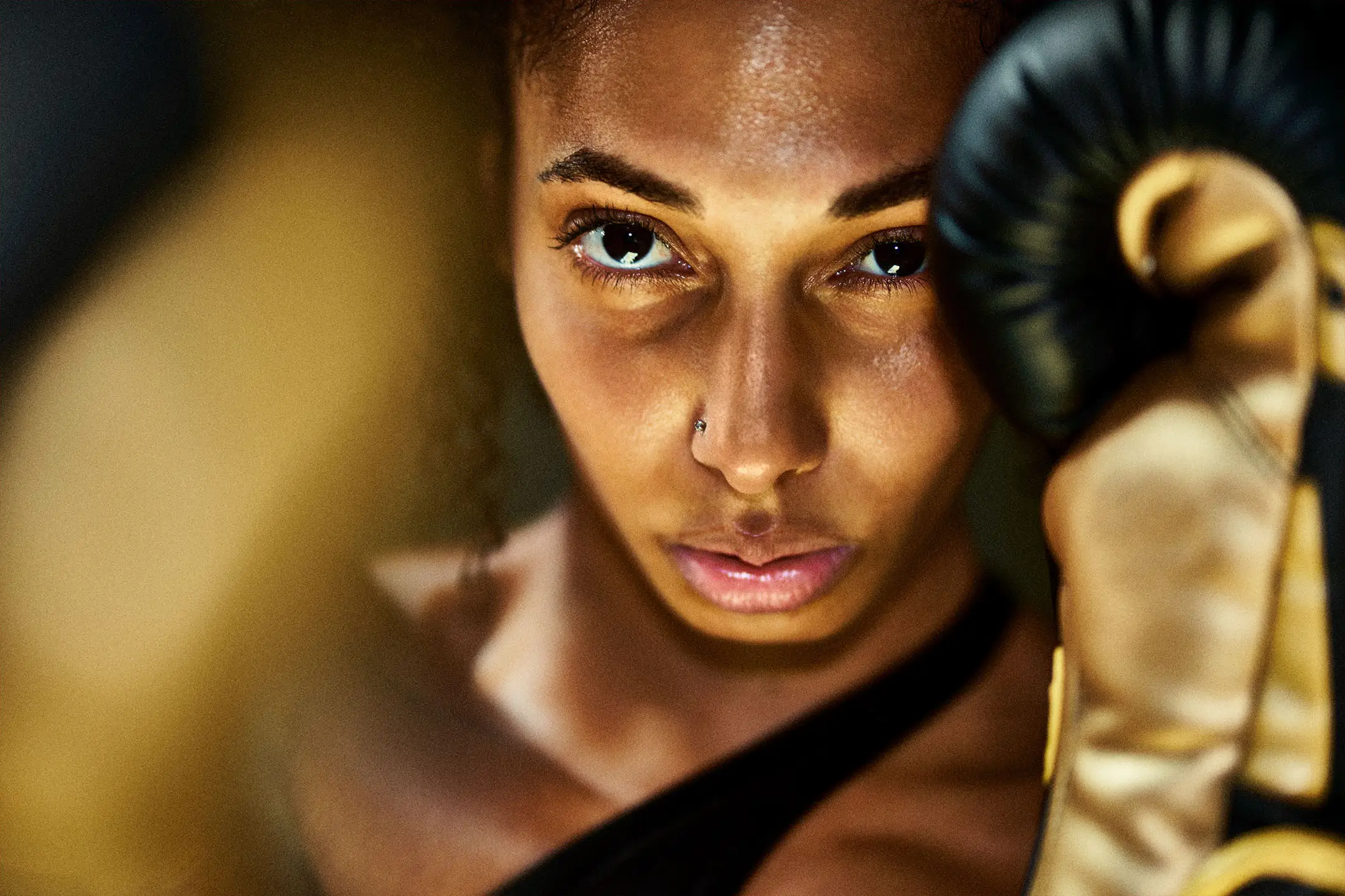 Close-up of focused female boxer wearing black and gold gloves in a defensive stance.