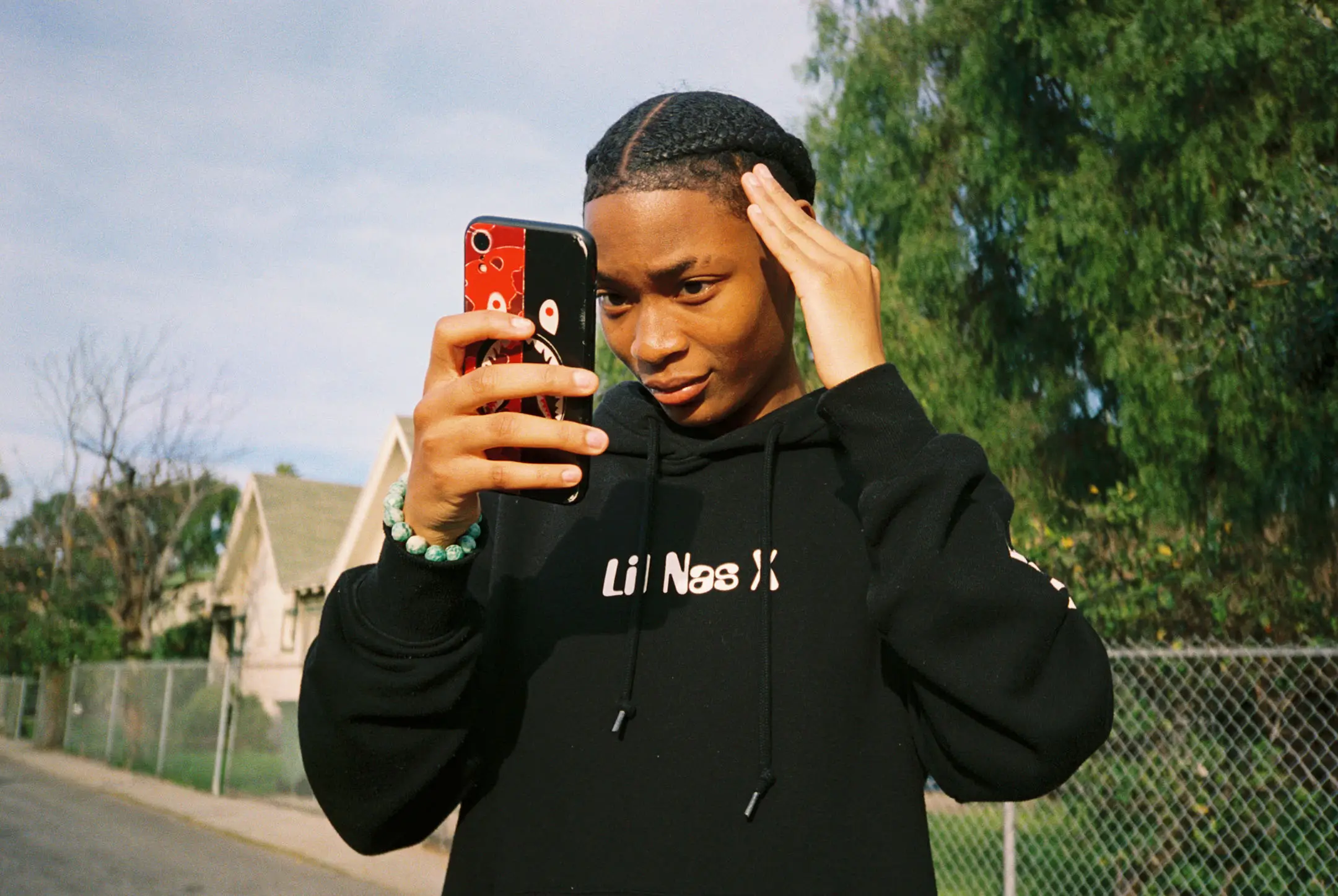 Person in a black hoodie taking a selfie outdoors with a phone in a red and black case.