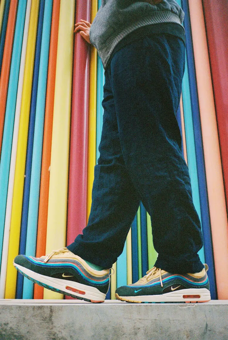 Person wearing multicolored Nike Air Max sneakers standing in front of a colorful vertical pipe wall.