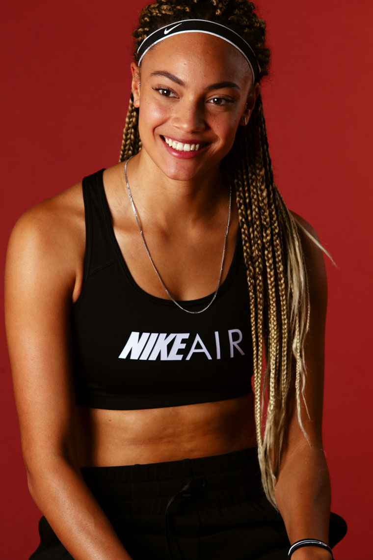Smiling woman wearing a black Nike Air sports bra and a black Nike headband against a red background.