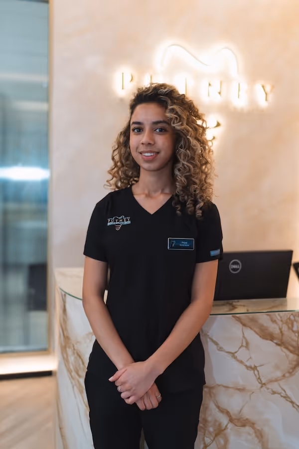 Smiling woman with curly hair wearing a black uniform standing behind a marble reception desk with a laptop.